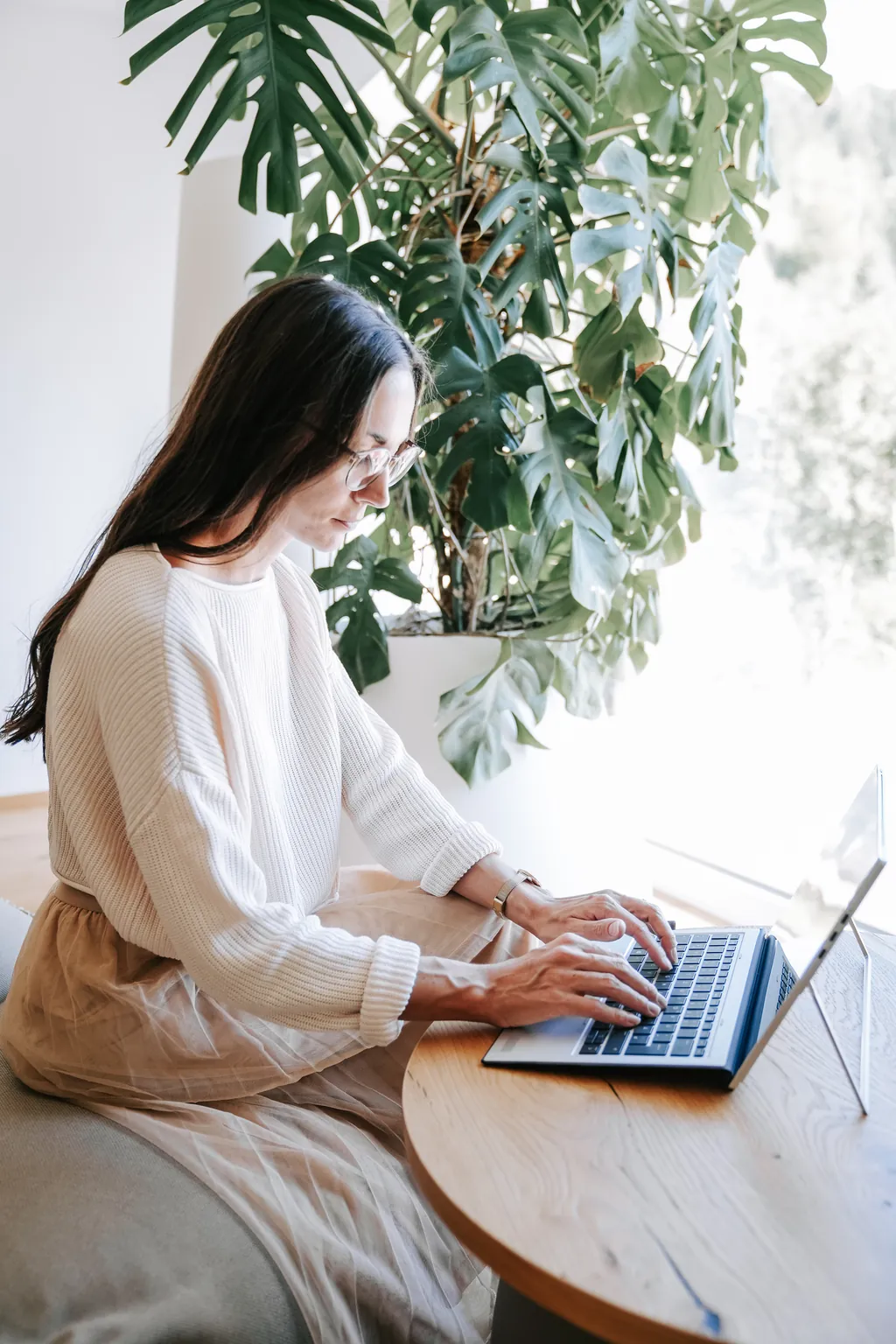 Sophie arbeitet am Laptop an einem Holztisch, hinter ihr eine große Monstera